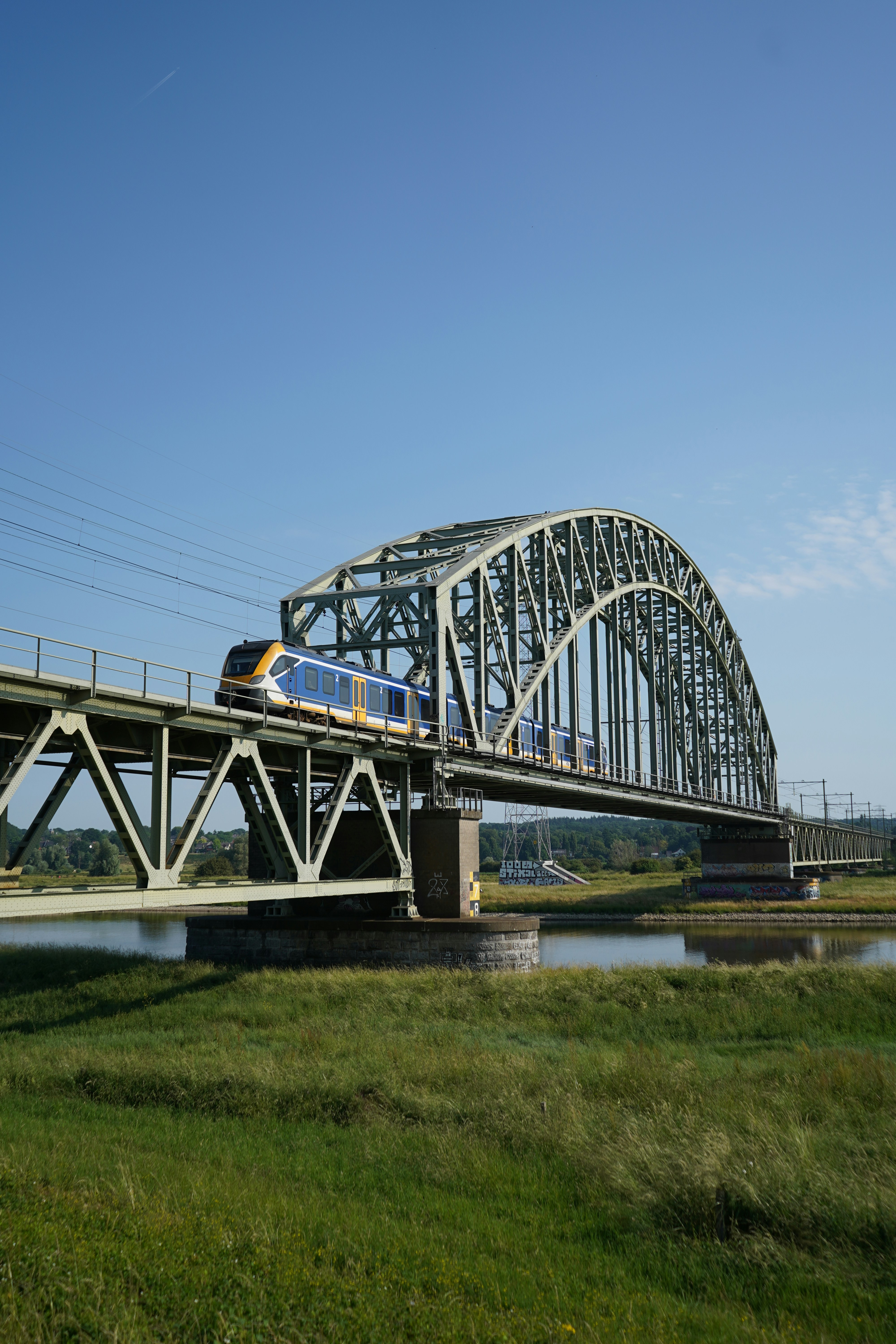 Nederlandse Spoorwegen trein op iconische stalen boogbrug over water, representatief voor RailGuard's expertise in Nederlandse spoorweginfrastructuur